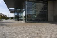 a walkway with glass walls near some people and trees on the side of the building