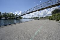 a metal bridge spanning over the water in a park area by a river and city skyline