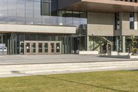 a grassy area with stairs leading to a building that has lots of windows and glass on the outside