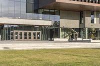 a grassy area with stairs leading to a building that has lots of windows and glass on the outside