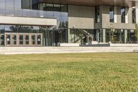 a grassy area with stairs leading to a building that has lots of windows and glass on the outside