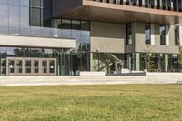 a grassy area with stairs leading to a building that has lots of windows and glass on the outside