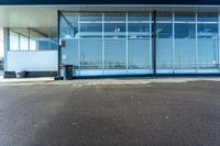 a parking lot with glass doors next to it and a bench under the building that has it's reflection in the window