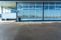 a parking lot with glass doors next to it and a bench under the building that has it's reflection in the window