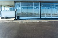 a parking lot with glass doors next to it and a bench under the building that has it's reflection in the window