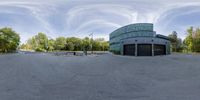 a panorama of an empty parking lot with a parking garage in the background and trees lining it