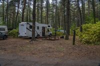 a couple of vehicles are parked near a camper trailer in a forest area with picnic tables and two caravans