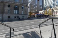 a metal handrail on the side of an empty street next to buildings and a bus