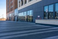 a sidewalk is lined with cement and large windows, with cars on the side of it