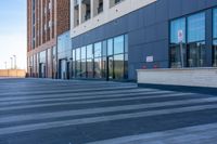 a sidewalk is lined with cement and large windows, with cars on the side of it