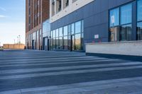 a sidewalk is lined with cement and large windows, with cars on the side of it