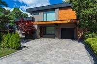 a two story, modern home with a wooden accent and a spacious driveway in front of a brick wall