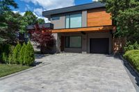 a two story, modern home with a wooden accent and a spacious driveway in front of a brick wall