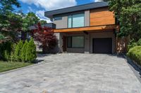 a two story, modern home with a wooden accent and a spacious driveway in front of a brick wall