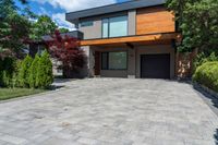 a two story, modern home with a wooden accent and a spacious driveway in front of a brick wall