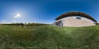 a 360 - view looking image of a house in a field of grass and a sky with clouds