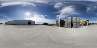 several barrels in the sand outside of an industrial building, with cloudy skies and sunlight