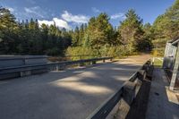 benches along a cement road near a lake, pine trees, and a building in the background