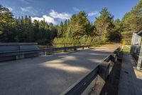 benches along a cement road near a lake, pine trees, and a building in the background