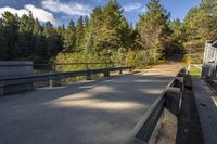 benches along a cement road near a lake, pine trees, and a building in the background