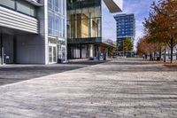 a cobblestone sidewalk is in front of a modern office building with glass windows and bales