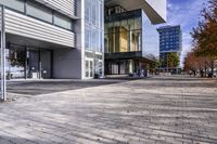 a cobblestone sidewalk is in front of a modern office building with glass windows and bales