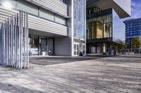 a cobblestone sidewalk is in front of a modern office building with glass windows and bales