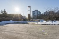 an empty parking lot is pictured in the sun with some snow on the ground and trees