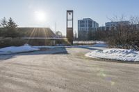 an empty parking lot is pictured in the sun with some snow on the ground and trees