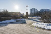 an empty parking lot is pictured in the sun with some snow on the ground and trees