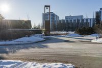 an empty parking lot is pictured in the sun with some snow on the ground and trees