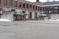 the empty parking lot has only snow on the ground in front of an old brick factory