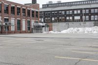 the empty parking lot has only snow on the ground in front of an old brick factory