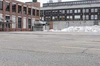 the empty parking lot has only snow on the ground in front of an old brick factory