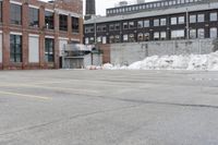 the empty parking lot has only snow on the ground in front of an old brick factory