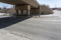 an empty street under a bridge next to an intersection with two people sitting on benches