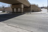 an empty street under a bridge next to an intersection with two people sitting on benches