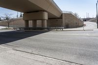 an empty street under a bridge next to an intersection with two people sitting on benches