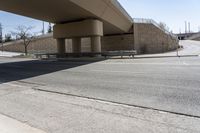 an empty street under a bridge next to an intersection with two people sitting on benches