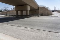 an empty street under a bridge next to an intersection with two people sitting on benches