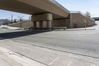 an empty street under a bridge next to an intersection with two people sitting on benches