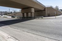 an empty street under a bridge next to an intersection with two people sitting on benches