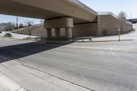 an empty street under a bridge next to an intersection with two people sitting on benches