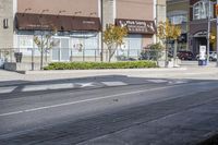 a woman on a bike is waiting to cross the street at an intersection, in front of stores