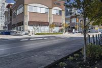 a woman on a bike is waiting to cross the street at an intersection, in front of stores