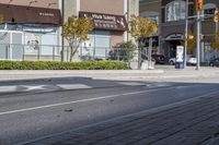 a woman on a bike is waiting to cross the street at an intersection, in front of stores