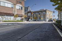 a woman on a bike is waiting to cross the street at an intersection, in front of stores