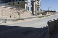 a city street lined with tall building next to an empty sidewalk and stone fence with benches near the sidewalk