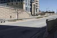 a city street lined with tall building next to an empty sidewalk and stone fence with benches near the sidewalk