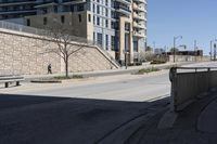 a city street lined with tall building next to an empty sidewalk and stone fence with benches near the sidewalk